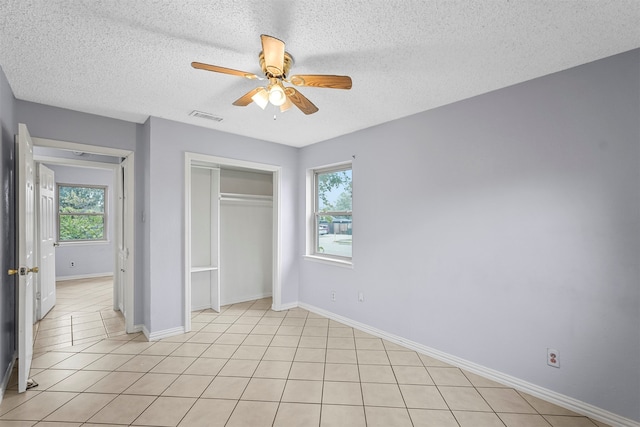 unfurnished bedroom featuring ceiling fan, multiple windows, light tile patterned floors, and a textured ceiling