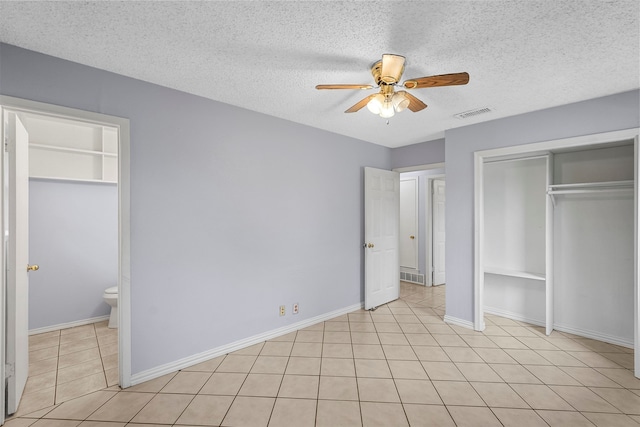 unfurnished bedroom featuring ensuite bath, a textured ceiling, ceiling fan, light tile patterned flooring, and a closet