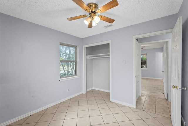 unfurnished bedroom with light tile patterned floors, ceiling fan, multiple windows, and a closet