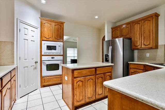 kitchen featuring white appliances, light tile patterned floors, backsplash, and a kitchen island