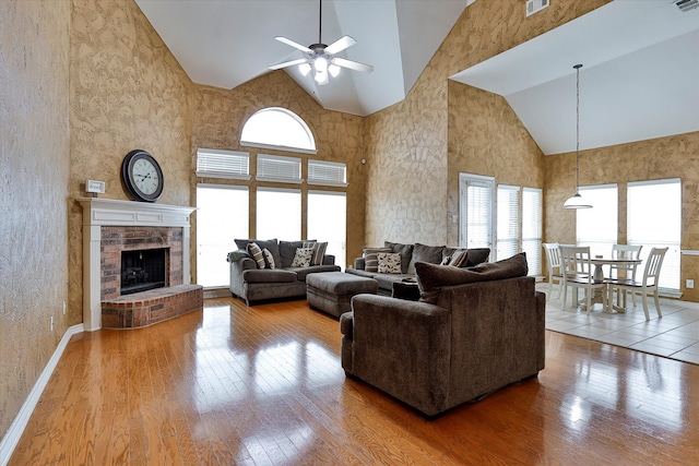 living room featuring high vaulted ceiling, a fireplace, hardwood / wood-style flooring, and ceiling fan