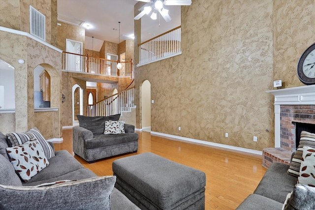 living room featuring a brick fireplace, a high ceiling, ceiling fan, and hardwood / wood-style flooring