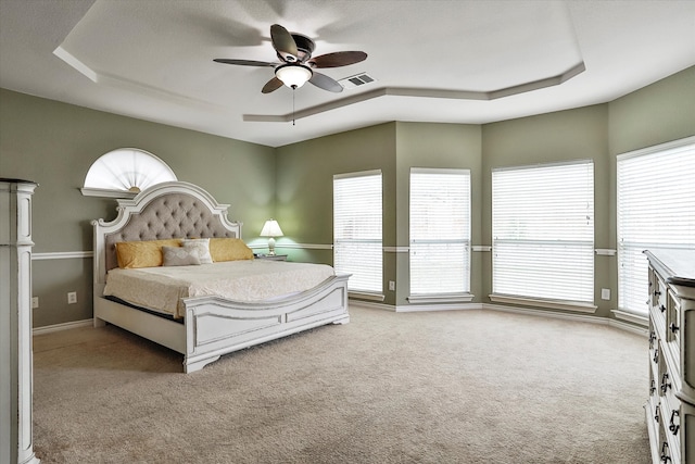 carpeted bedroom featuring multiple windows, a raised ceiling, and ceiling fan