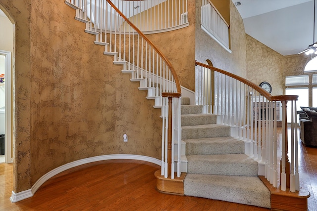 stairs with high vaulted ceiling, hardwood / wood-style floors, and ceiling fan