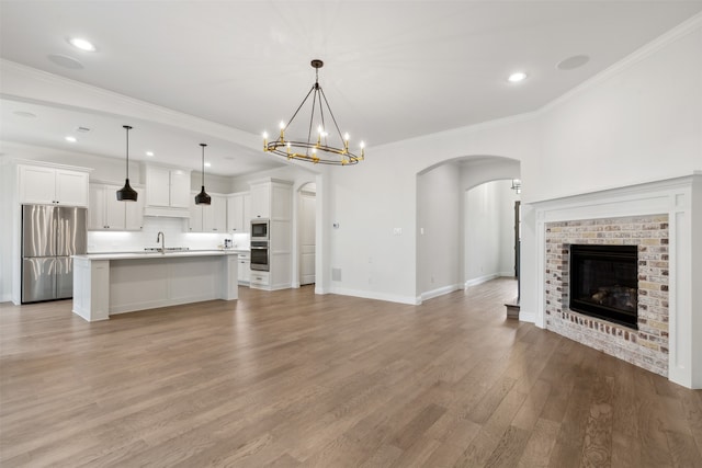 unfurnished living room featuring a brick fireplace, light hardwood / wood-style floors, sink, and crown molding