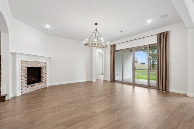 unfurnished living room with light wood-type flooring, a fireplace, a notable chandelier, and crown molding