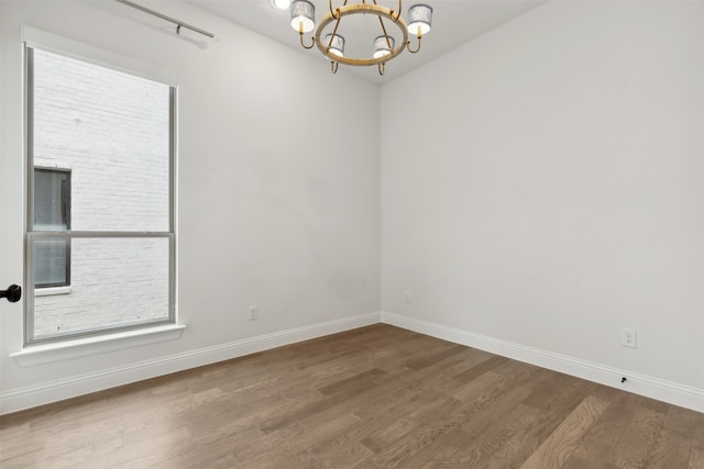 empty room with wood-type flooring and a notable chandelier