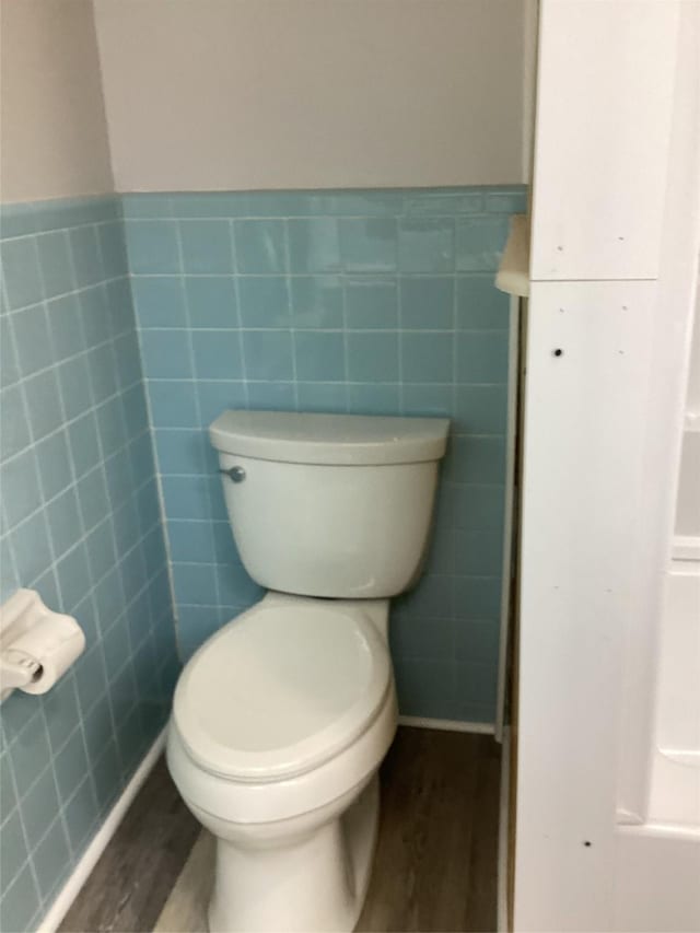 604 S Seaman St, Eastland, TX 76448 - bathroom with wood finished floors, tile walls, toilet, and a wainscoted wall