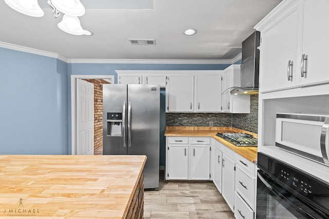 kitchen featuring wooden counters, stainless steel appliances, wall chimney exhaust hood, ornamental molding, and white cabinetry