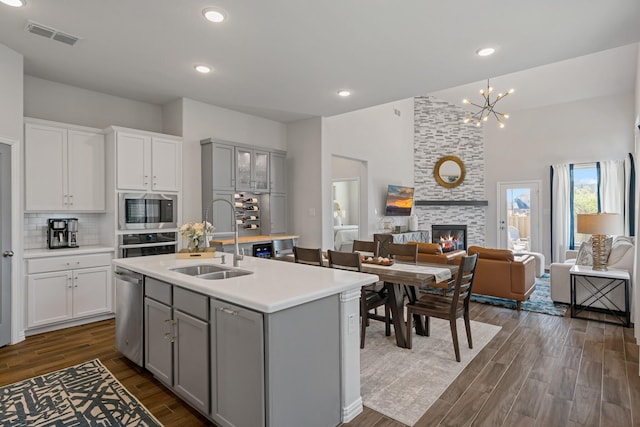 kitchen featuring a stone fireplace, appliances with stainless steel finishes, gray cabinetry, tasteful backsplash, and sink