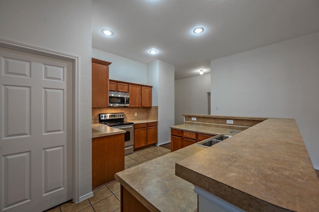 kitchen with stainless steel appliances, kitchen peninsula, sink, tasteful backsplash, and light tile patterned flooring