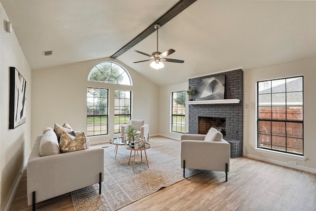 living room with a brick fireplace, light hardwood / wood-style flooring, vaulted ceiling with beams, and ceiling fan