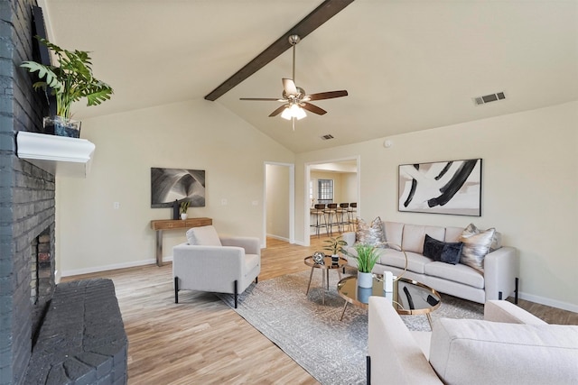 living room featuring a fireplace, ceiling fan, light hardwood / wood-style flooring, and vaulted ceiling with beams