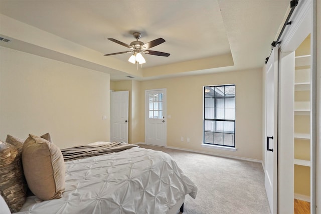 carpeted bedroom featuring a barn door, ceiling fan, and a raised ceiling