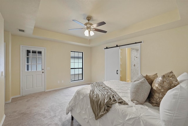 carpeted bedroom featuring a tray ceiling, a barn door, and ceiling fan