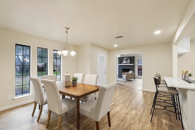 dining space with a fireplace, light hardwood / wood-style floors, and an inviting chandelier