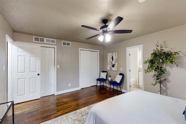 bedroom with dark hardwood / wood-style flooring, a textured ceiling, two closets, connected bathroom, and ceiling fan