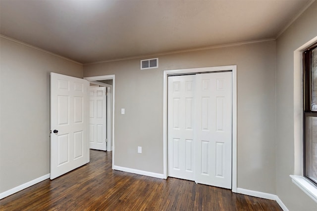 unfurnished bedroom with dark hardwood / wood-style flooring, crown molding, and a closet