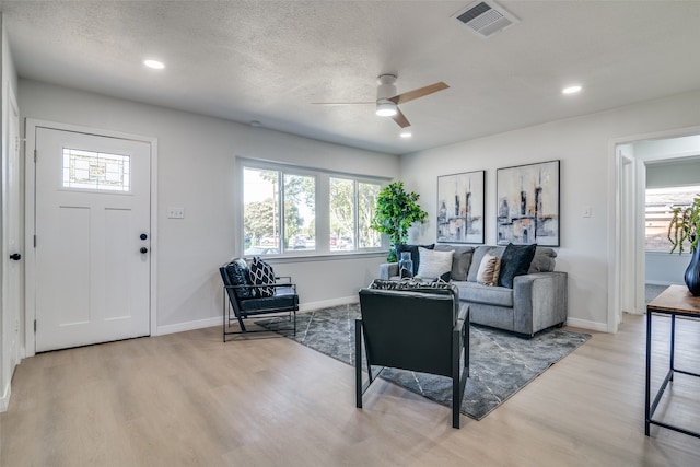 living room with ceiling fan, light hardwood / wood-style floors, and a textured ceiling