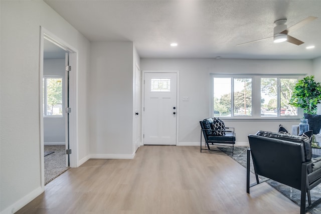 foyer entrance featuring a textured ceiling, light hardwood / wood-style flooring, a wealth of natural light, and ceiling fan