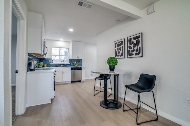 kitchen with stainless steel appliances, tasteful backsplash, a breakfast bar area, white cabinets, and light wood-type flooring