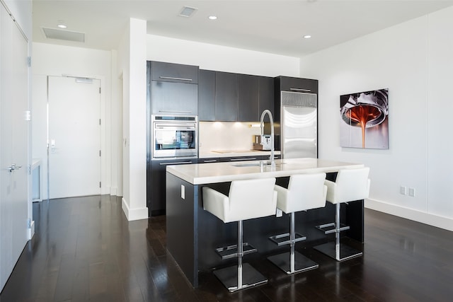 kitchen with tasteful backsplash, a center island with sink, stainless steel appliances, dark hardwood / wood-style flooring, and a breakfast bar area