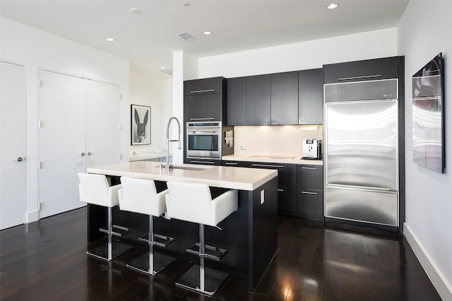 kitchen with dark wood-type flooring, a breakfast bar area, sink, a kitchen island with sink, and appliances with stainless steel finishes