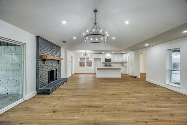 unfurnished living room featuring lofted ceiling, light wood-type flooring, a fireplace, and a chandelier