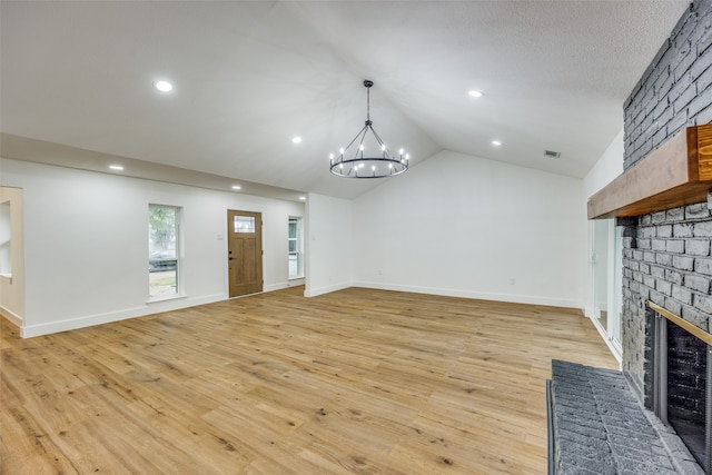 unfurnished living room with a brick fireplace, a textured ceiling, an inviting chandelier, light hardwood / wood-style floors, and lofted ceiling