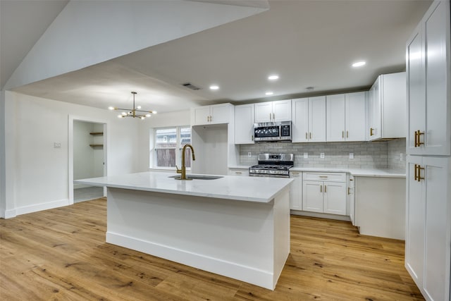 kitchen with appliances with stainless steel finishes, sink, a center island with sink, light hardwood / wood-style flooring, and white cabinets