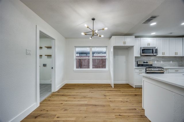 kitchen featuring a notable chandelier, pendant lighting, light hardwood / wood-style floors, white cabinets, and appliances with stainless steel finishes