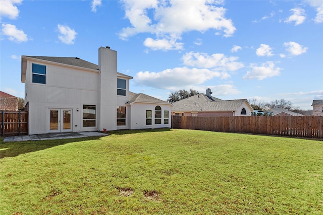 rear view of property with a fenced backyard, french doors, a chimney, and a yard