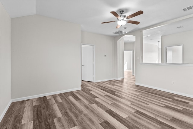 unfurnished room with light wood-style floors, arched walkways, visible vents, and baseboards