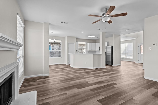 unfurnished living room with visible vents, a fireplace with flush hearth, wood finished floors, and ceiling fan with notable chandelier