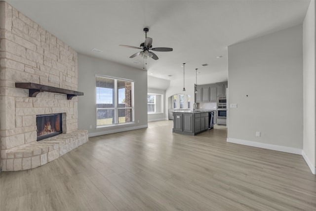 unfurnished living room featuring ceiling fan, sink, light wood-type flooring, and a fireplace