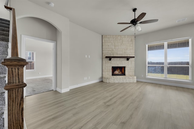 unfurnished living room with plenty of natural light, light hardwood / wood-style floors, a stone fireplace, and ceiling fan