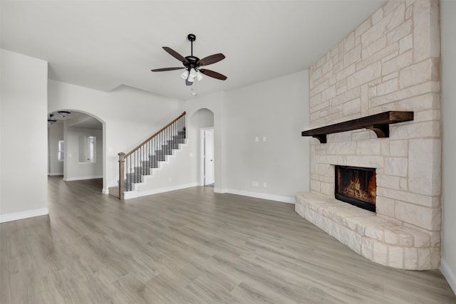 unfurnished living room with ceiling fan, light hardwood / wood-style floors, and a stone fireplace