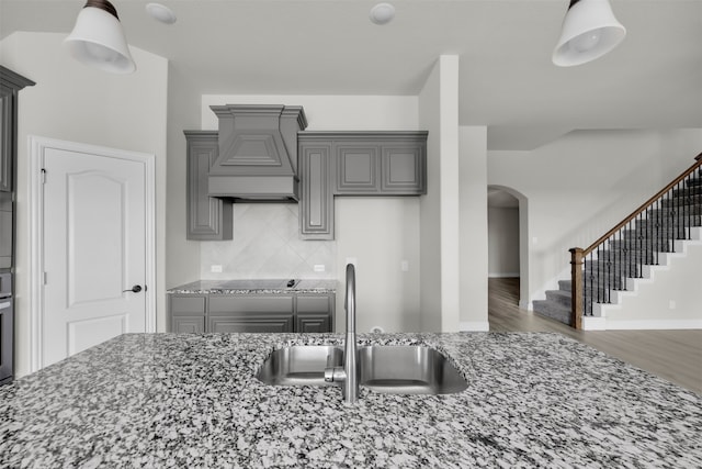 kitchen featuring light stone counters, custom range hood, dark wood-type flooring, sink, and gray cabinets