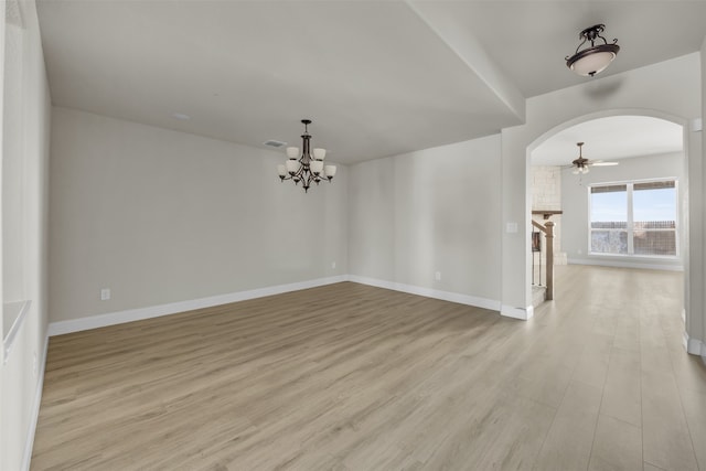 spare room with ceiling fan with notable chandelier, light wood-type flooring, and a stone fireplace