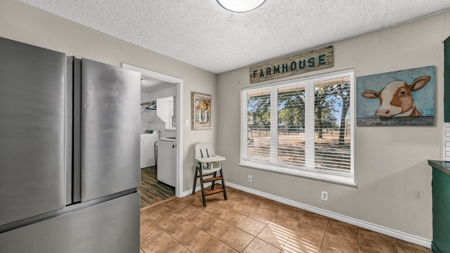 kitchen featuring washer and clothes dryer, tile patterned flooring, a textured ceiling, and stainless steel refrigerator