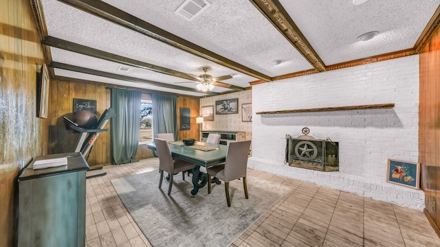 dining area featuring a fireplace, beamed ceiling, wood walls, and a textured ceiling