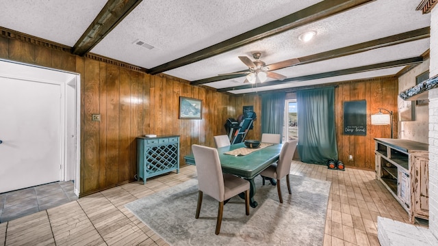 dining area featuring wood walls, a textured ceiling, ceiling fan, and beam ceiling