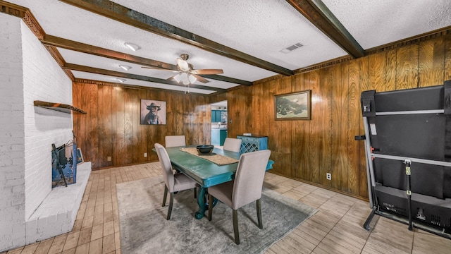 dining space featuring ceiling fan, beamed ceiling, a textured ceiling, and wooden walls