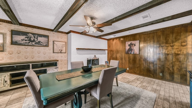 tiled dining area featuring a textured ceiling, wood walls, beamed ceiling, and ceiling fan