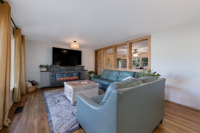 living room with a stone fireplace, ceiling fan, and light hardwood / wood-style flooring