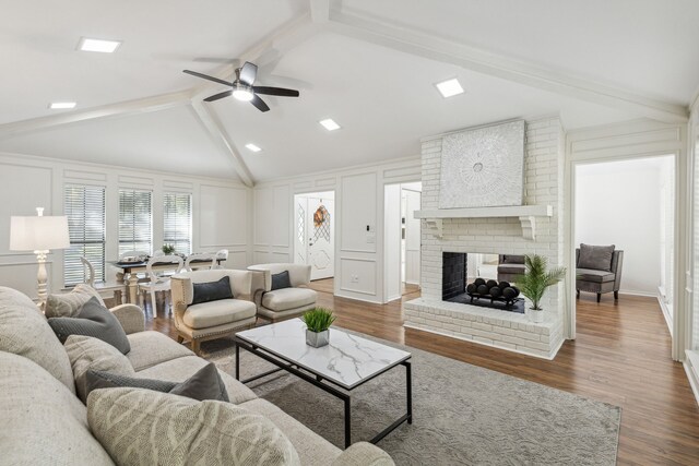 living room featuring dark wood-type flooring, ceiling fan, a fireplace, and lofted ceiling with beams