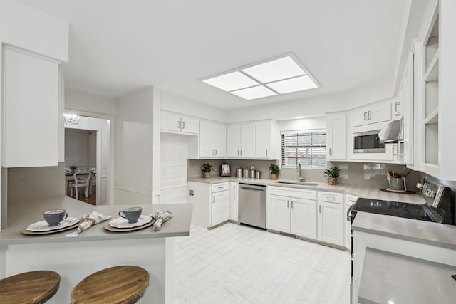 kitchen with appliances with stainless steel finishes, white cabinetry, sink, a kitchen bar, and kitchen peninsula