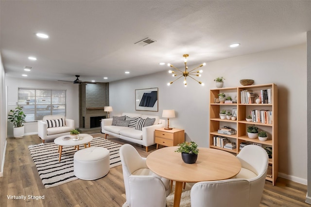 interior space featuring hardwood / wood-style floors, ceiling fan with notable chandelier, and a brick fireplace