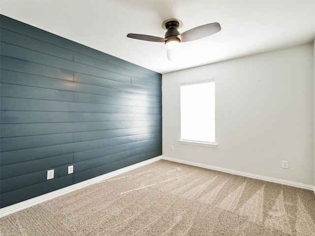 carpeted empty room featuring wood walls and ceiling fan