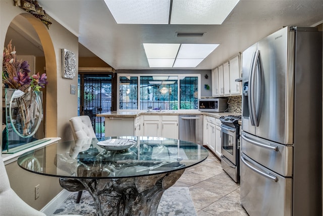 kitchen featuring stainless steel appliances, light stone counters, tasteful backsplash, light tile patterned floors, and white cabinets